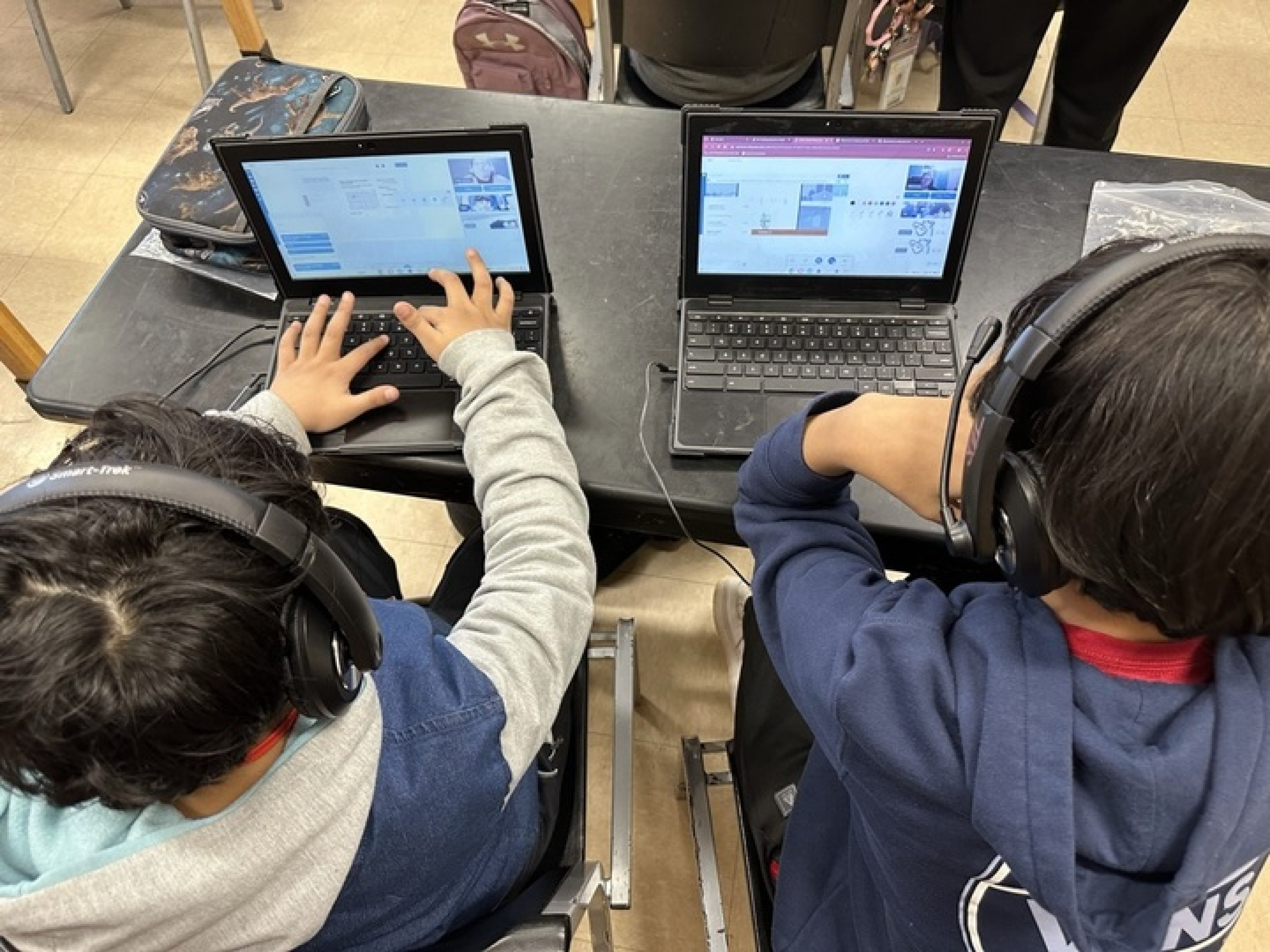 Students wearing headphones being tutored on laptops